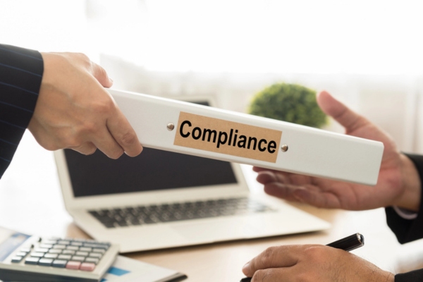 person passing a file folder labeled COMPLIANCE to another person