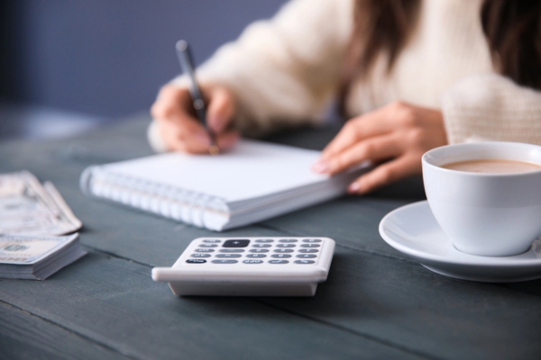 woman writing on her notepad with calculator, a stack of cash, and coffee determining propane use