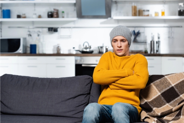 shivering man wearing a sweater and a beanie feeling cold indoors